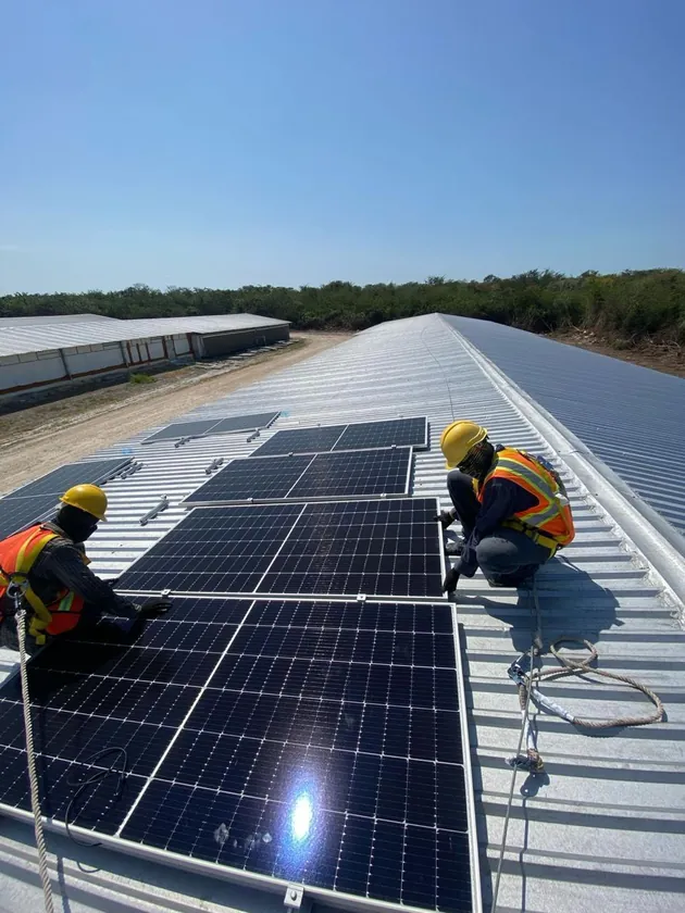 Dos instaladores con casco y chaleco colocando paneles solares en un techo de lámina