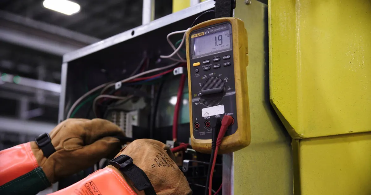 Técnico con guantes de protección midiendo con un multímetro en un tablero eléctrico